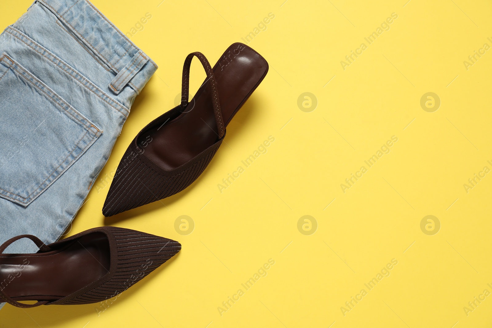 Photo of Stylish brown shoes and jeans on yellow background, flat lay. Space for text