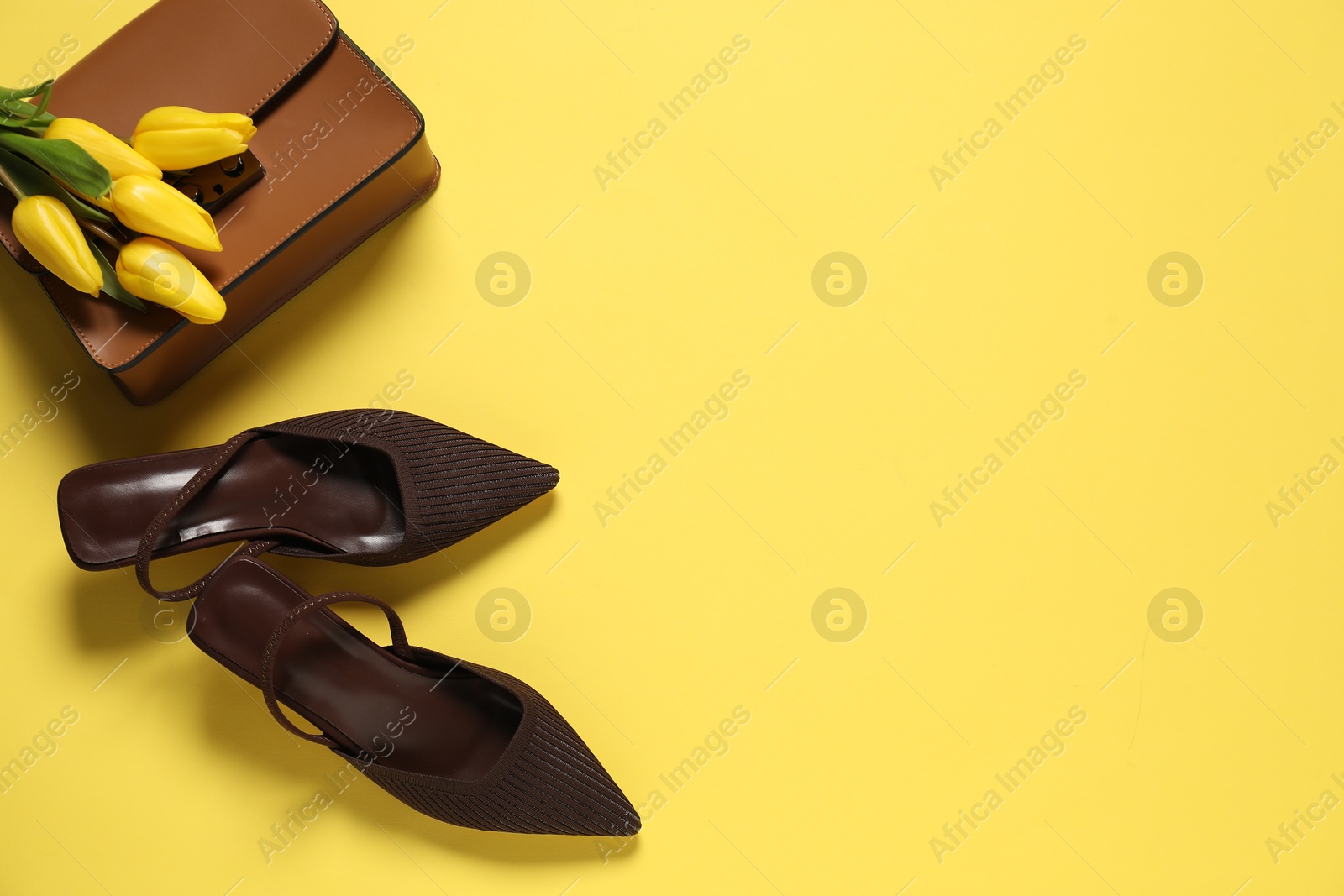 Photo of Stylish brown shoes, bag and tulips on yellow background, flat lay. Space for text