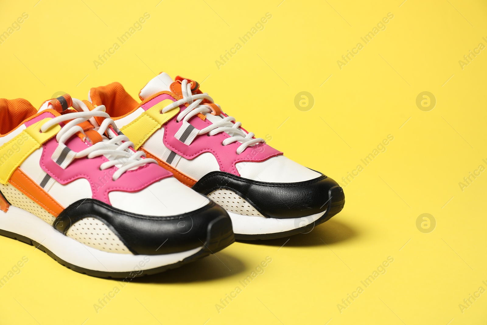 Photo of Stylish sneakers on yellow background. Sportive shoes