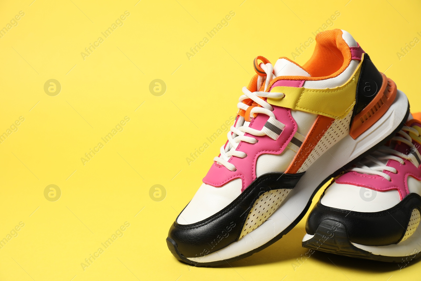 Photo of Sportive shoes. Stylish sneakers on yellow background, space for text