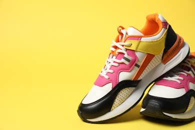 Photo of Sportive shoes. Stylish sneakers on yellow background, space for text