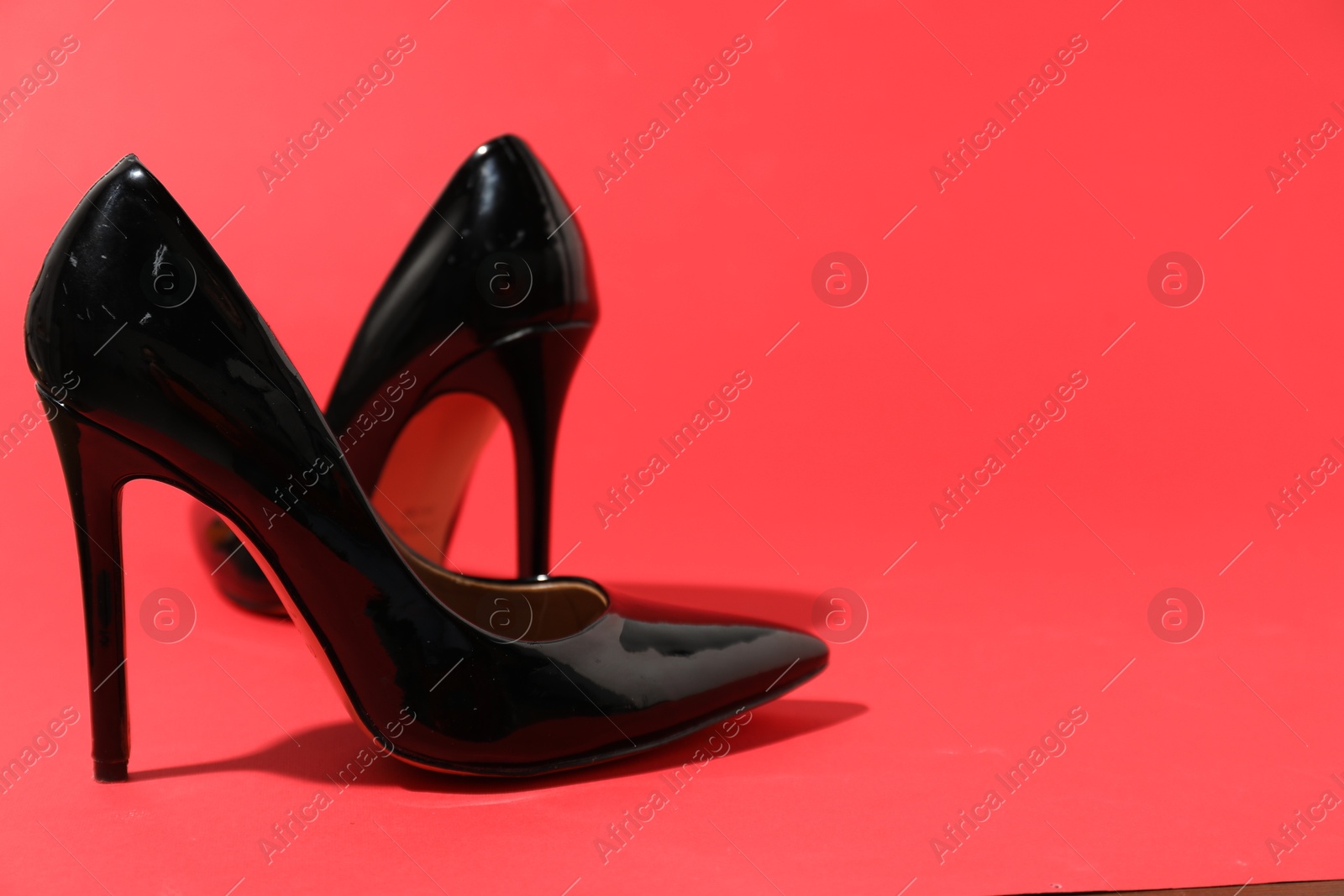 Photo of Black high heeled shoes on crimson background, space for text