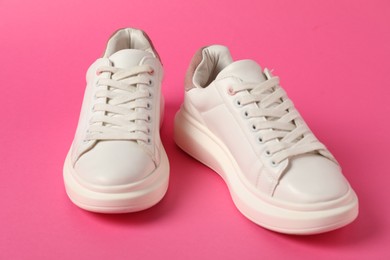 Photo of White sneakers on pink background, closeup. Sportive shoes