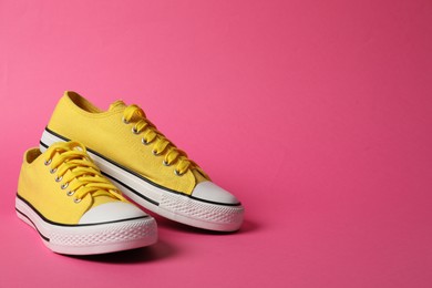 Photo of Sportive shoes. Yellow sneakers on pink background, space for text