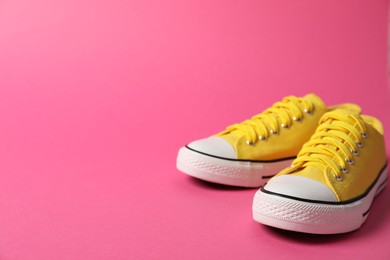 Photo of Sportive shoes. Yellow sneakers on pink background, space for text