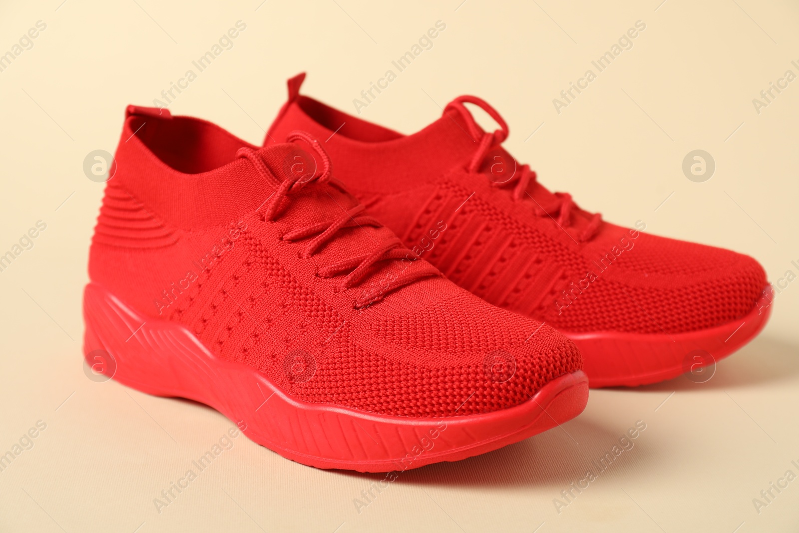 Photo of Red sneakers on beige background, closeup. Sportive shoes