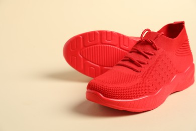 Photo of Sportive shoes. Red sneakers on beige background, closeup. Space for text