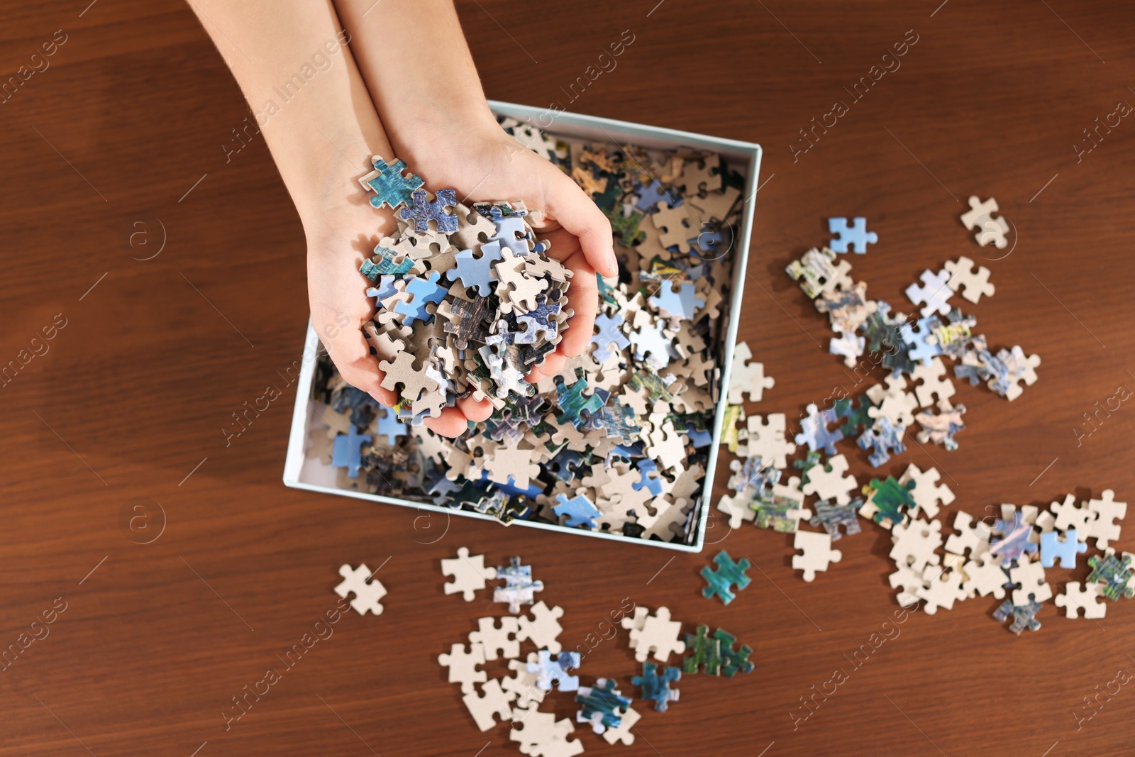 Photo of Girl with box of puzzle pieces at wooden table, top view