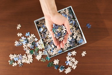 Photo of Man with box of puzzle pieces at wooden table, top view