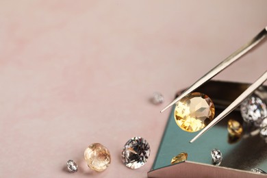 Photo of Tweezers with beautiful gemstones on light pink table, selective focus. Space for text