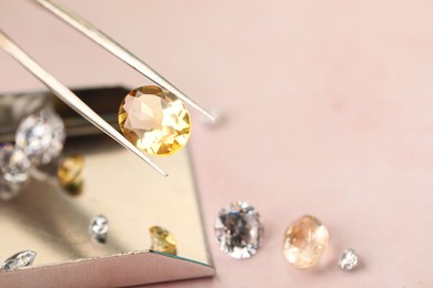 Photo of Tweezers with beautiful gemstones on light pink table, selective focus. Space for text