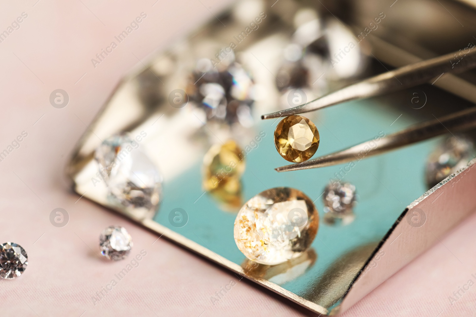 Photo of Tweezers with beautiful gemstones on light pink table, selective focus