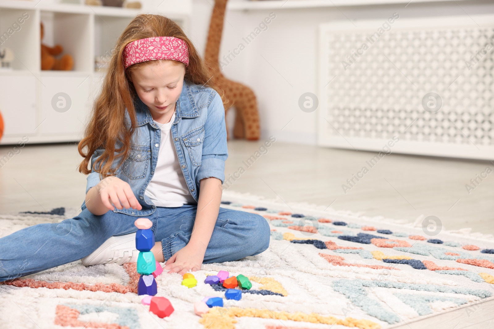 Photo of Little girl building tower with balancing stones on floor indoors, space for text