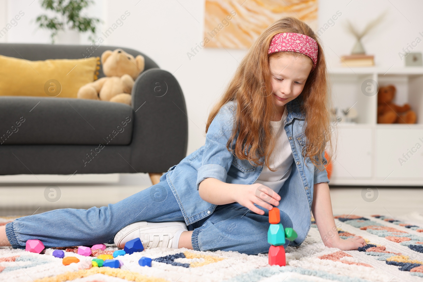 Photo of Little girl building tower with balancing stones on floor indoors