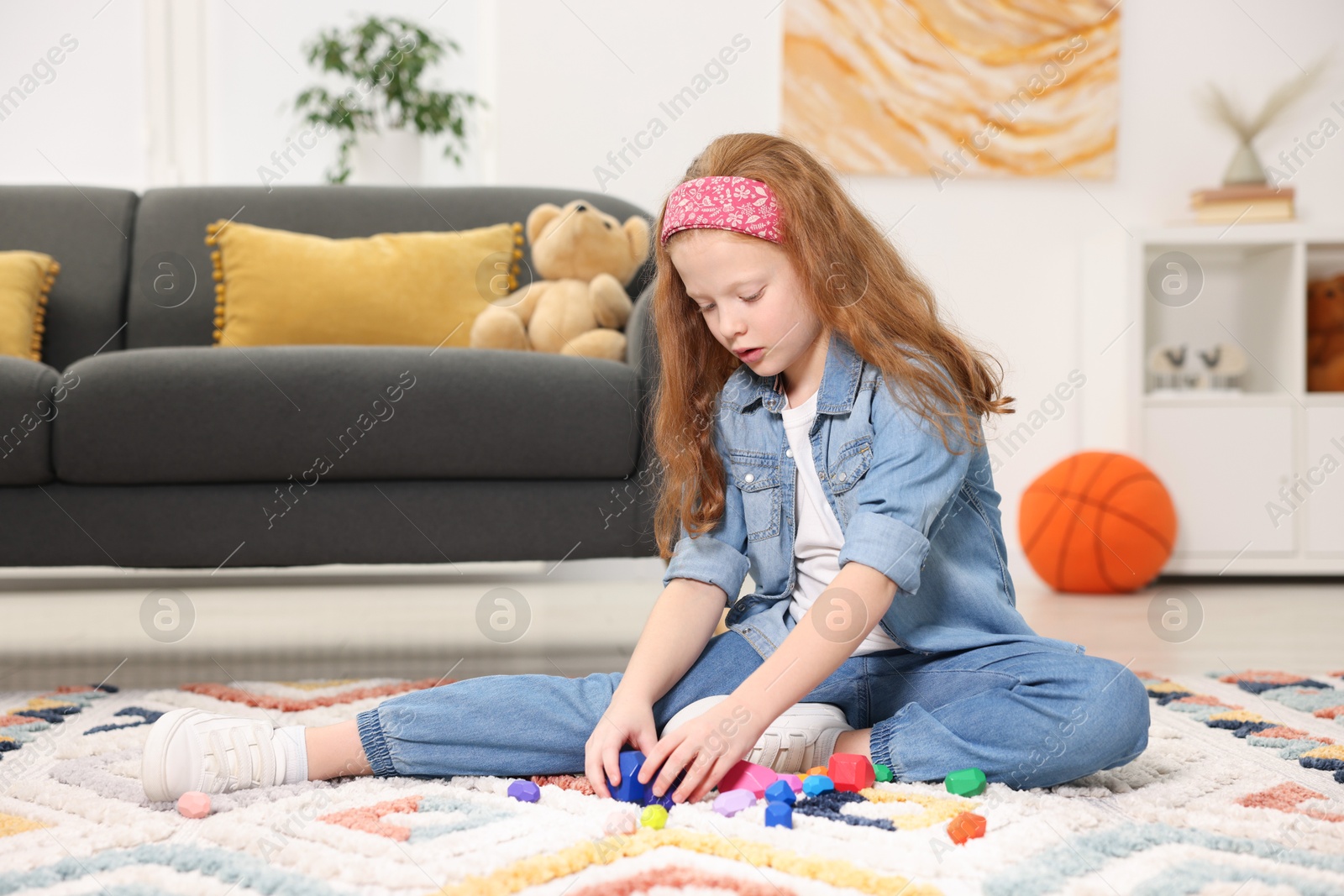 Photo of Little girl playing with balancing stones on floor indoors