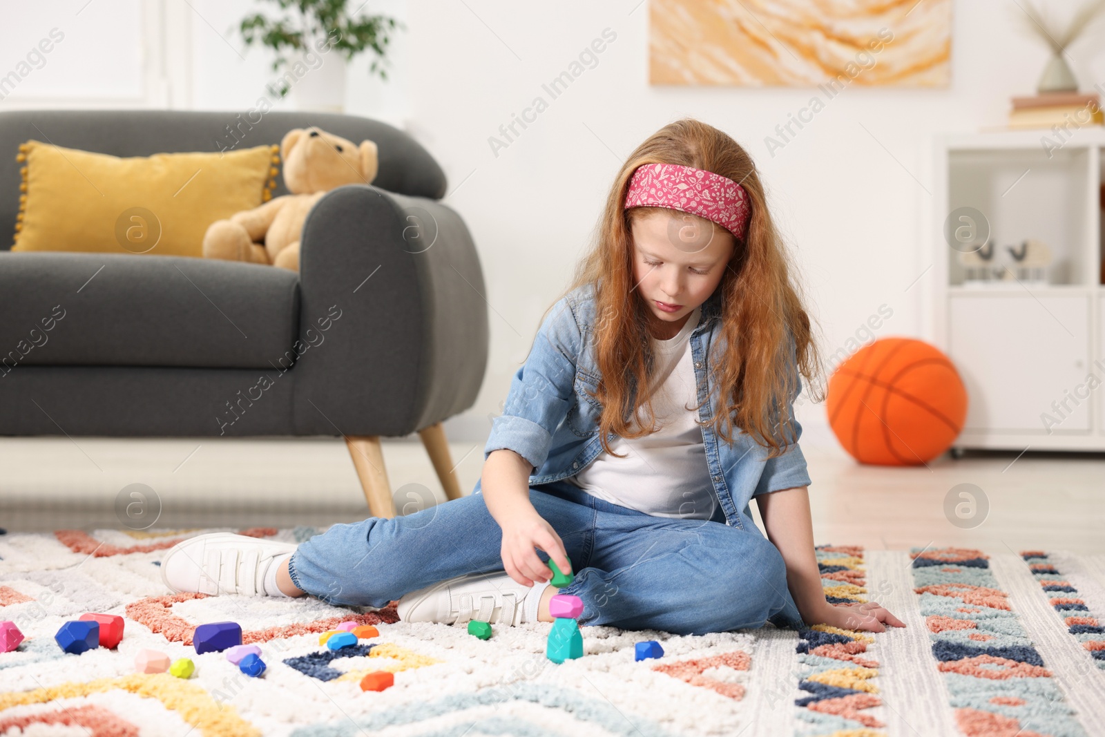 Photo of Little girl building tower with balancing stones on floor indoors