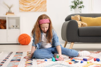 Photo of Little girl playing with balancing stones on floor indoors