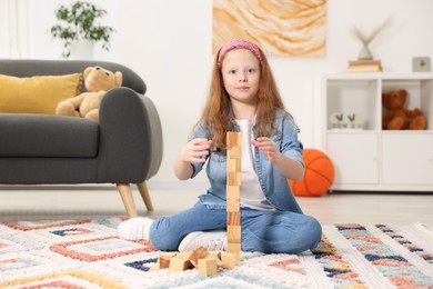 Photo of Little girl building tower with wooden cubes on floor indoors