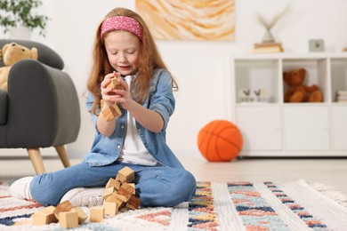 Photo of Little girl playing with wooden cubes on floor indoors, space for text