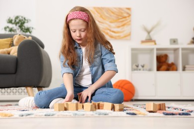 Photo of Little girl playing with wooden cubes on floor indoors, space for text