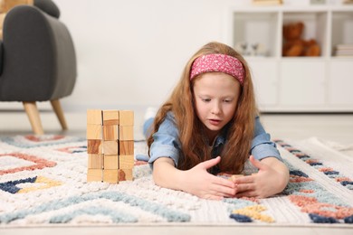 Photo of Little girl playing with wooden cubes on floor indoors