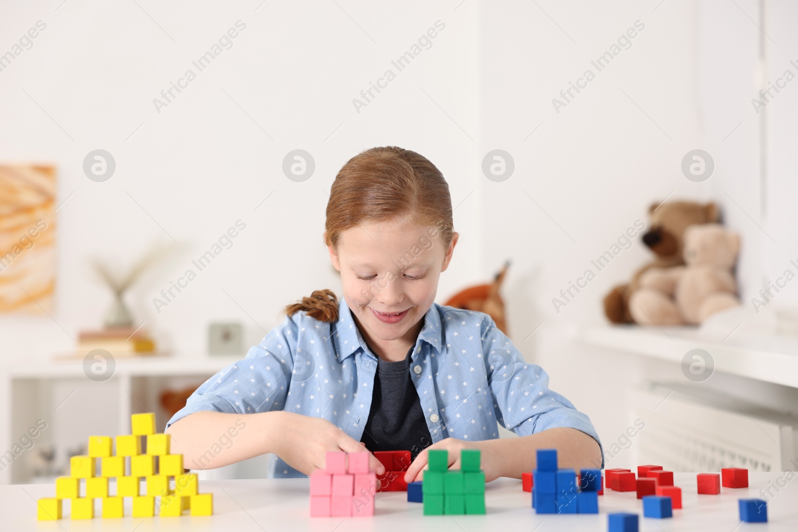 Photo of Little girl playing with colorful cubes at white table indoors