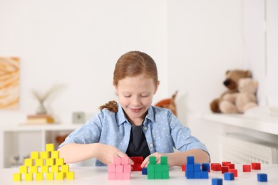 Photo of Little girl playing with colorful cubes at white table indoors