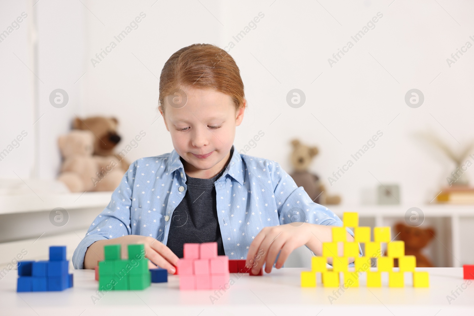 Photo of Little girl playing with colorful cubes at white table indoors