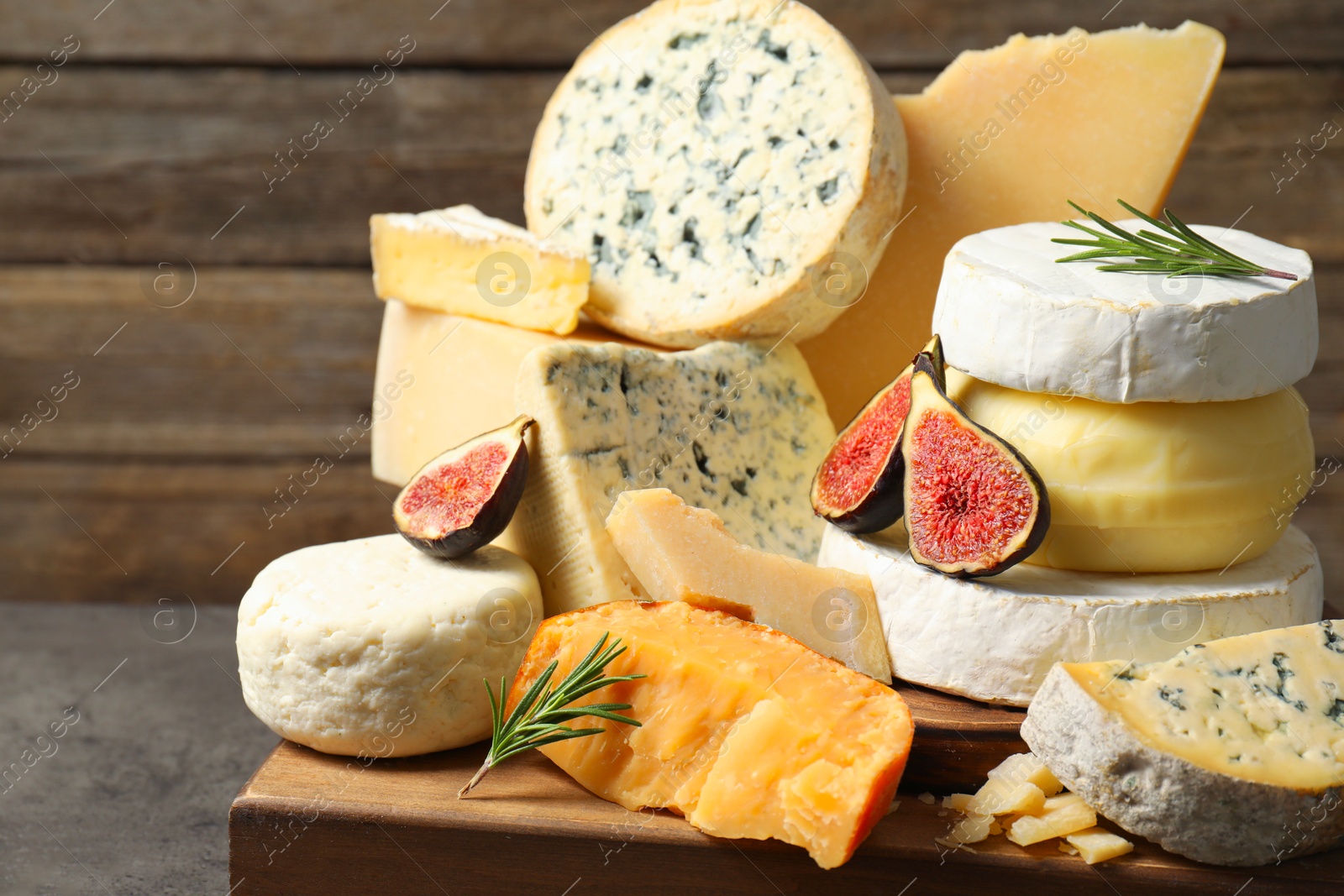 Photo of Different types of cheese, figs and rosemary on grey table, closeup