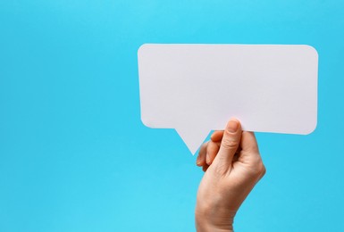 Photo of Woman holding blank speech bubble on light blue background, closeup. Space for text