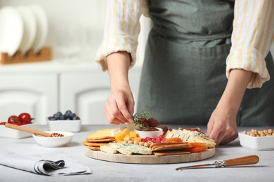 Photo of Woman serving antipasto platter with different types of cheese and other snacks with thyme at grey textured table indoors, closeup