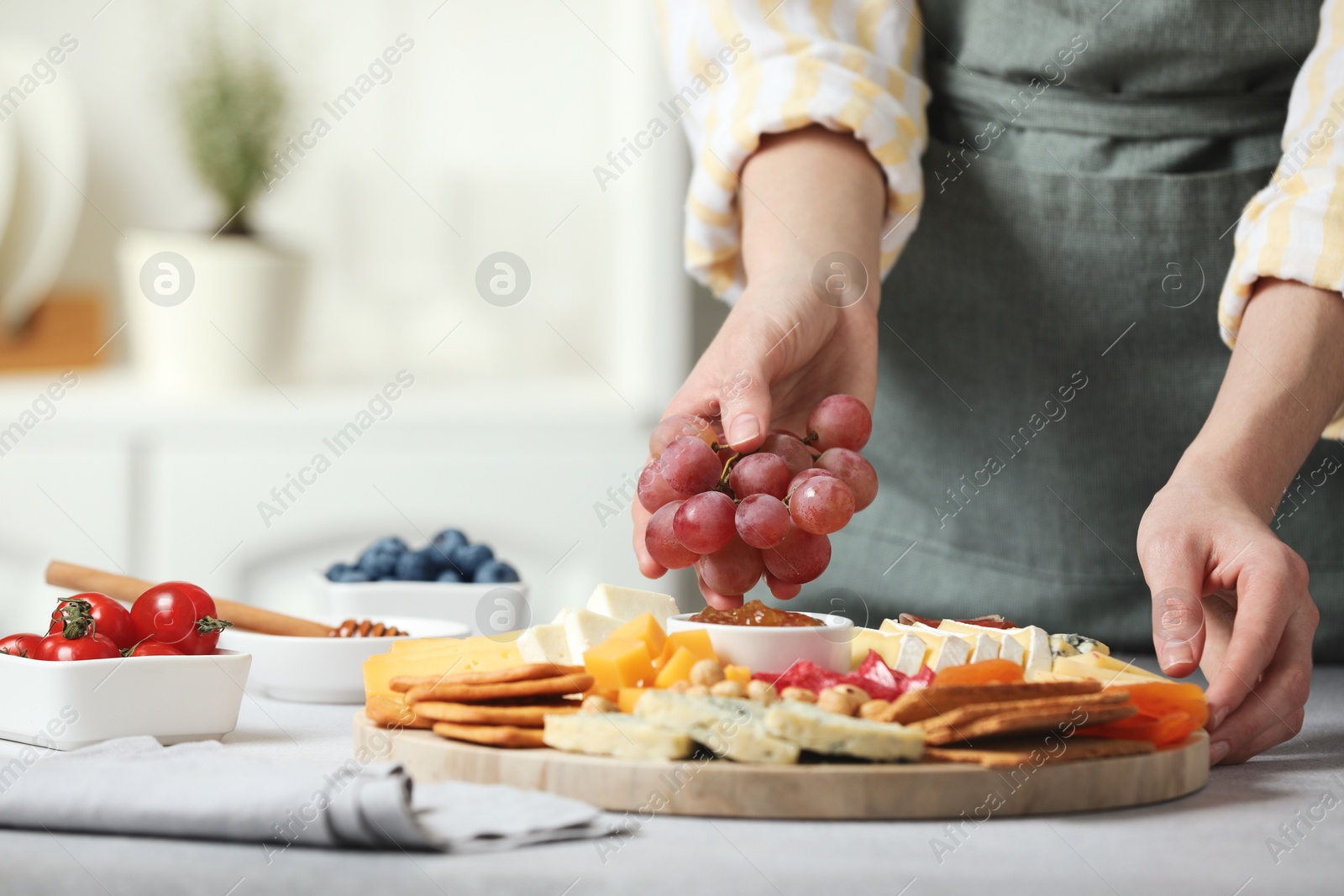 Photo of Woman serving antipasto platter with different types of cheese and other snacks with grapes at grey textured table indoors, closeup