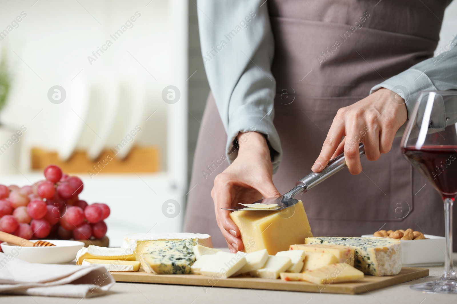 Photo of Woman slicing delicious cheese at light textured table indoors, closeup