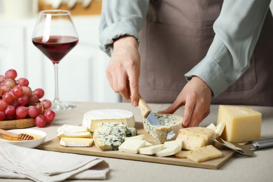 Photo of Woman slicing delicious cheese at light textured table indoors, closeup