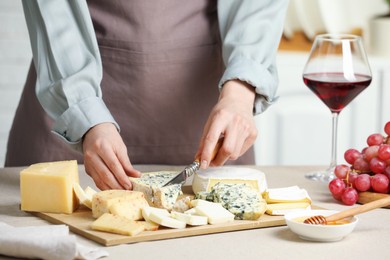 Photo of Woman slicing delicious cheese at light textured table indoors, closeup