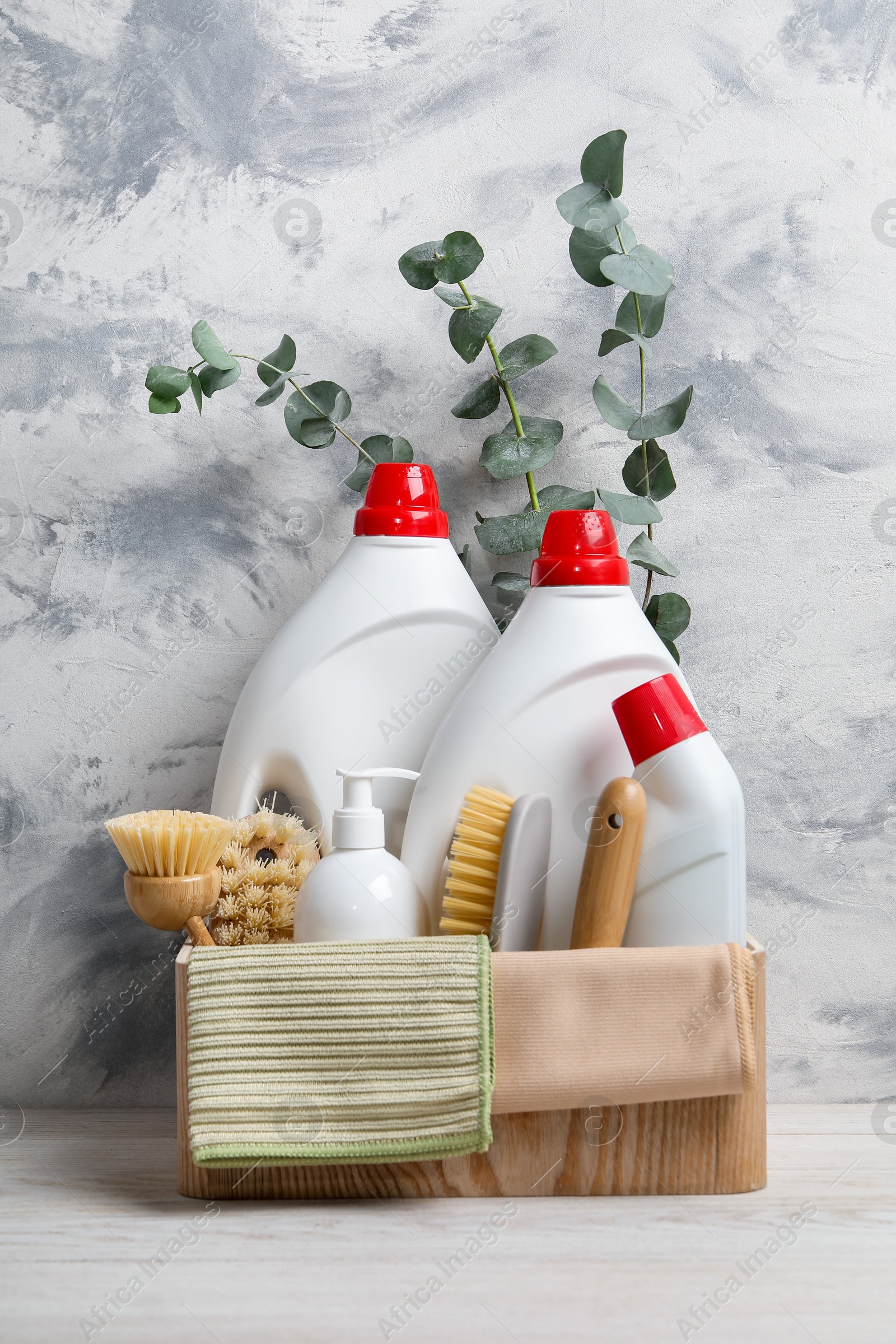 Photo of Eco-friendly cleaning products, supplies and eucalyptus branches in crate on light wooden table