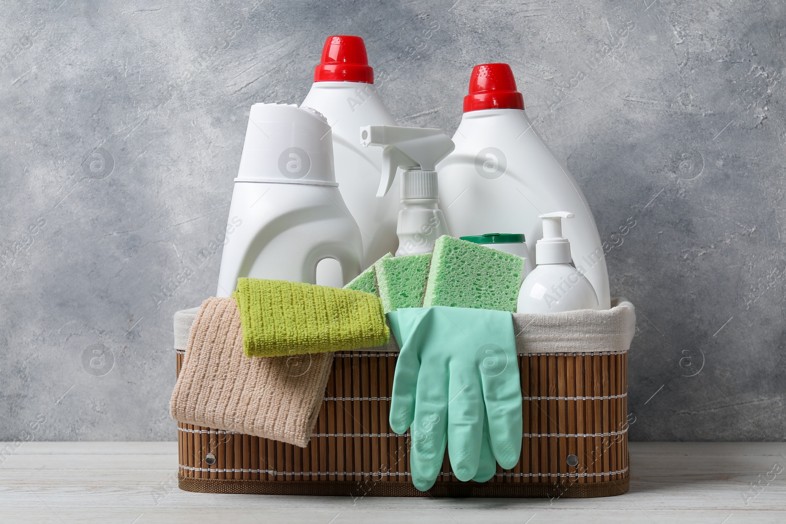 Photo of Eco-friendly cleaning products and supplies in wicker basket on light wooden table