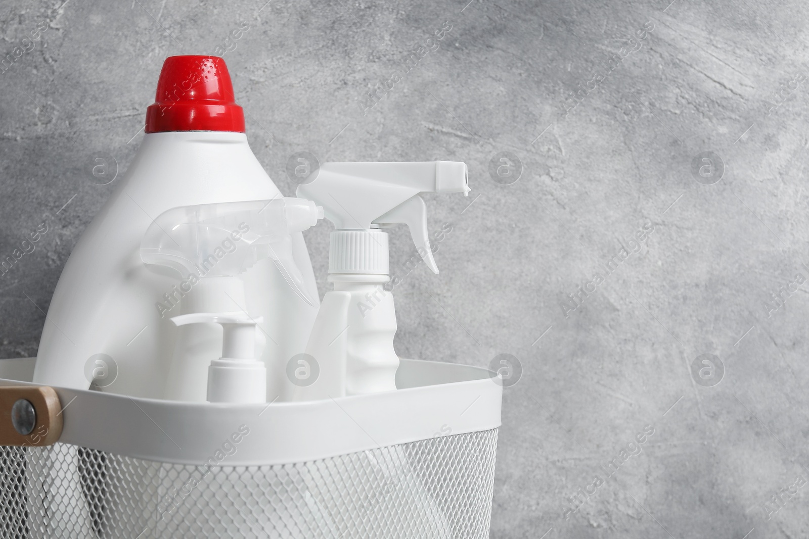 Photo of Different cleaning products in basket against grey background, closeup. Space for text