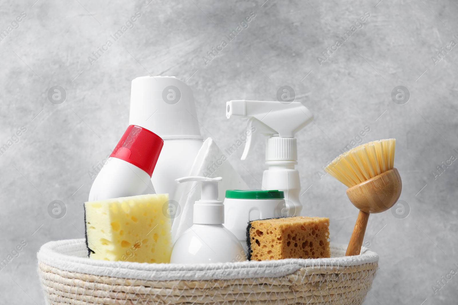 Photo of Eco-friendly cleaning products and supplies in wicker basket against grey background, closeup