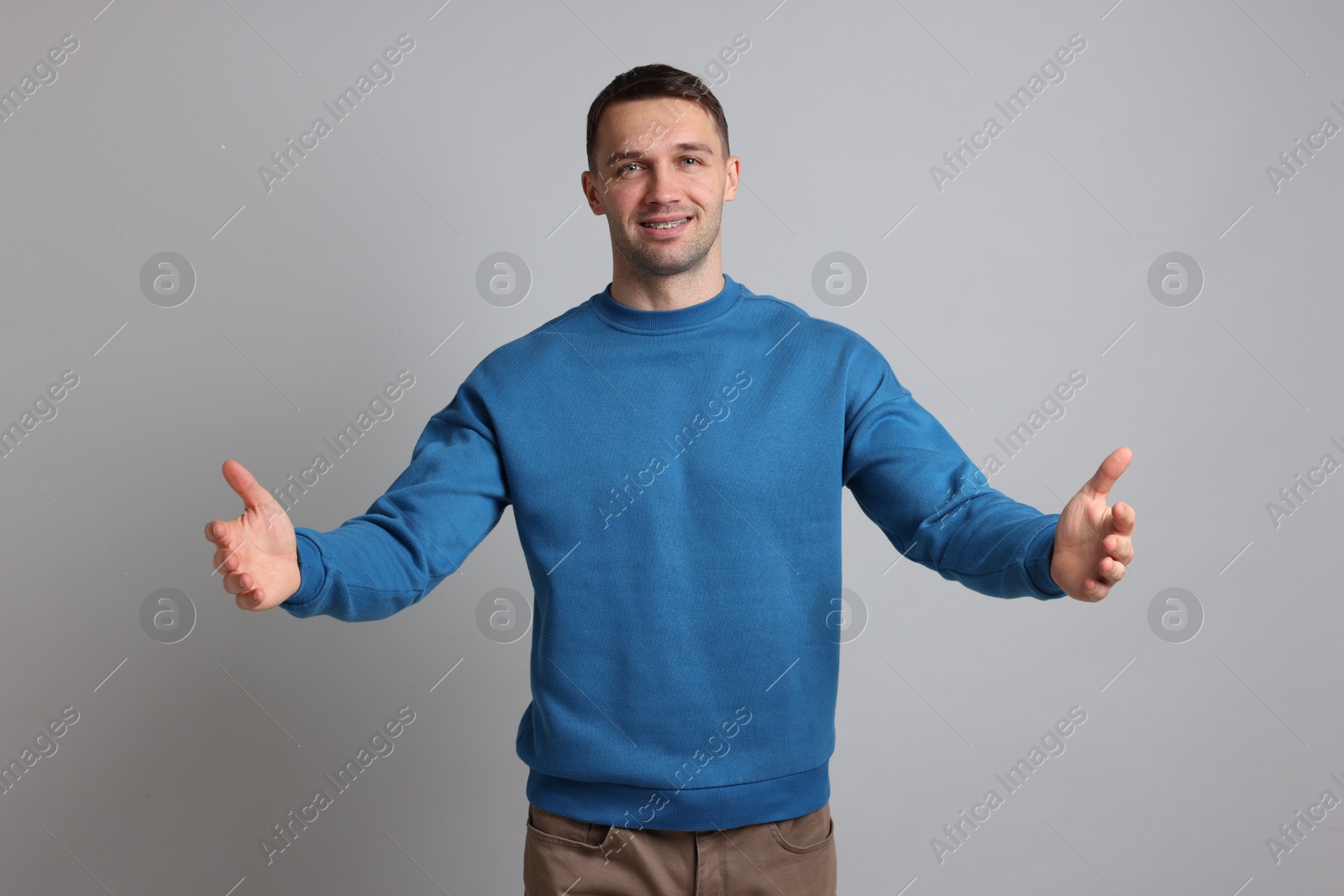 Photo of Cheerful man welcoming guests on light grey background