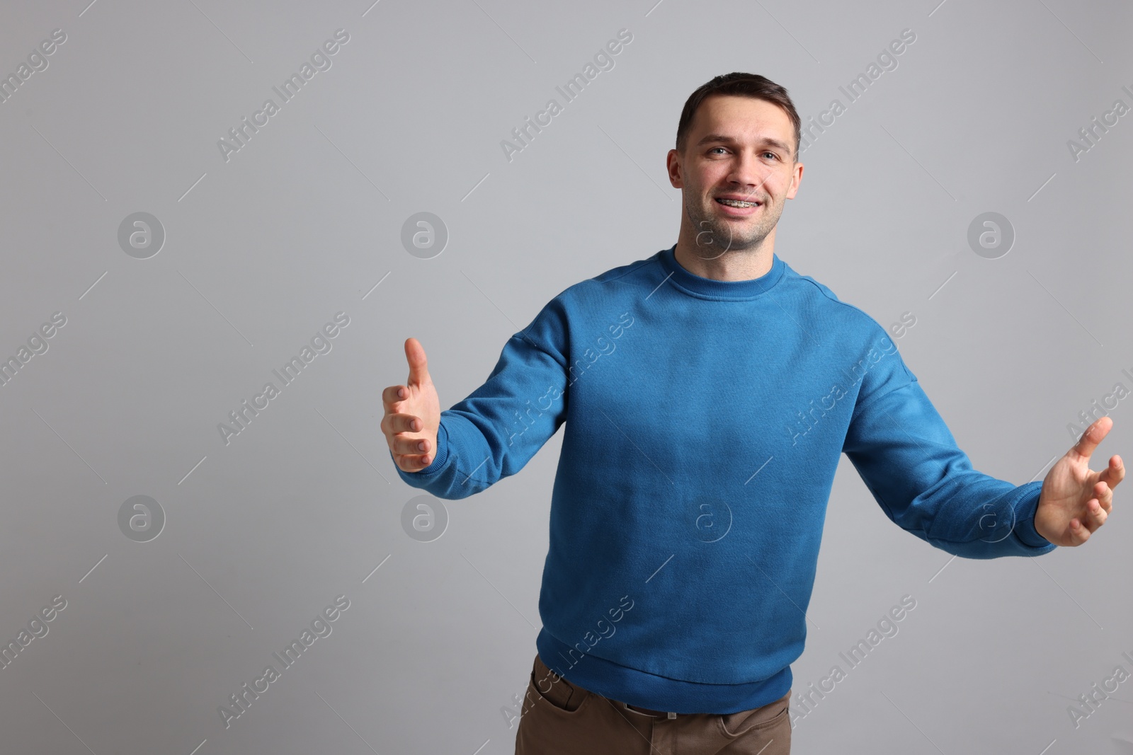 Photo of Cheerful man welcoming guests on light grey background