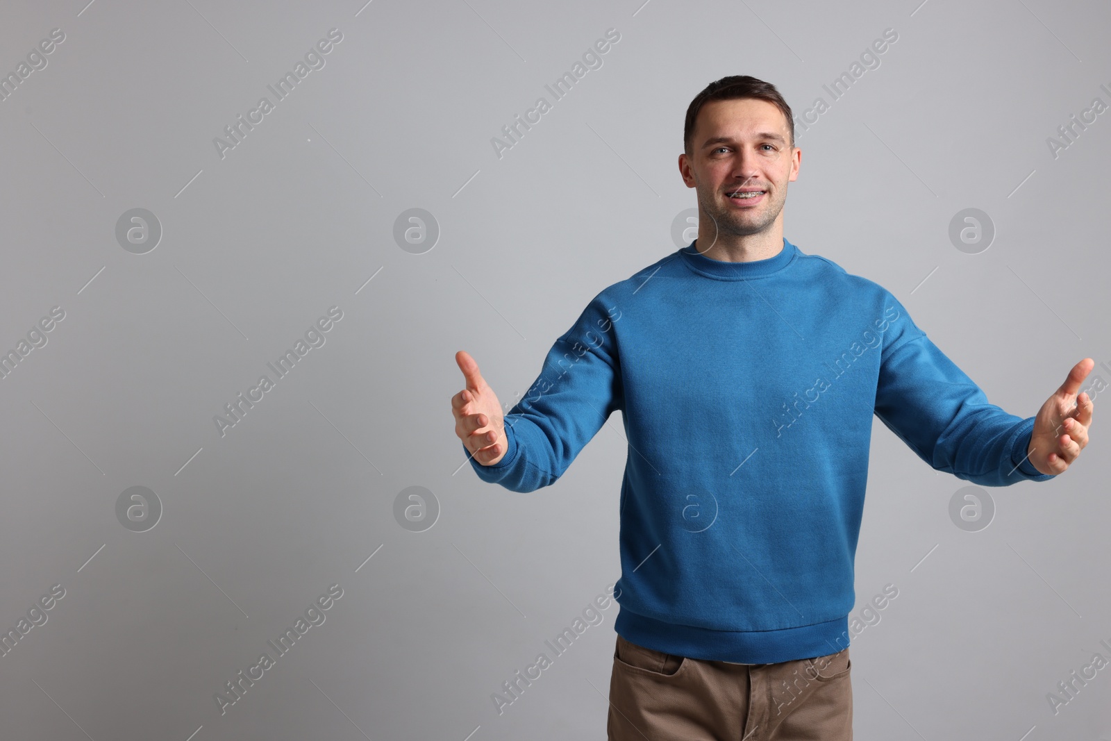 Photo of Cheerful man welcoming guests on light grey background. Space for text