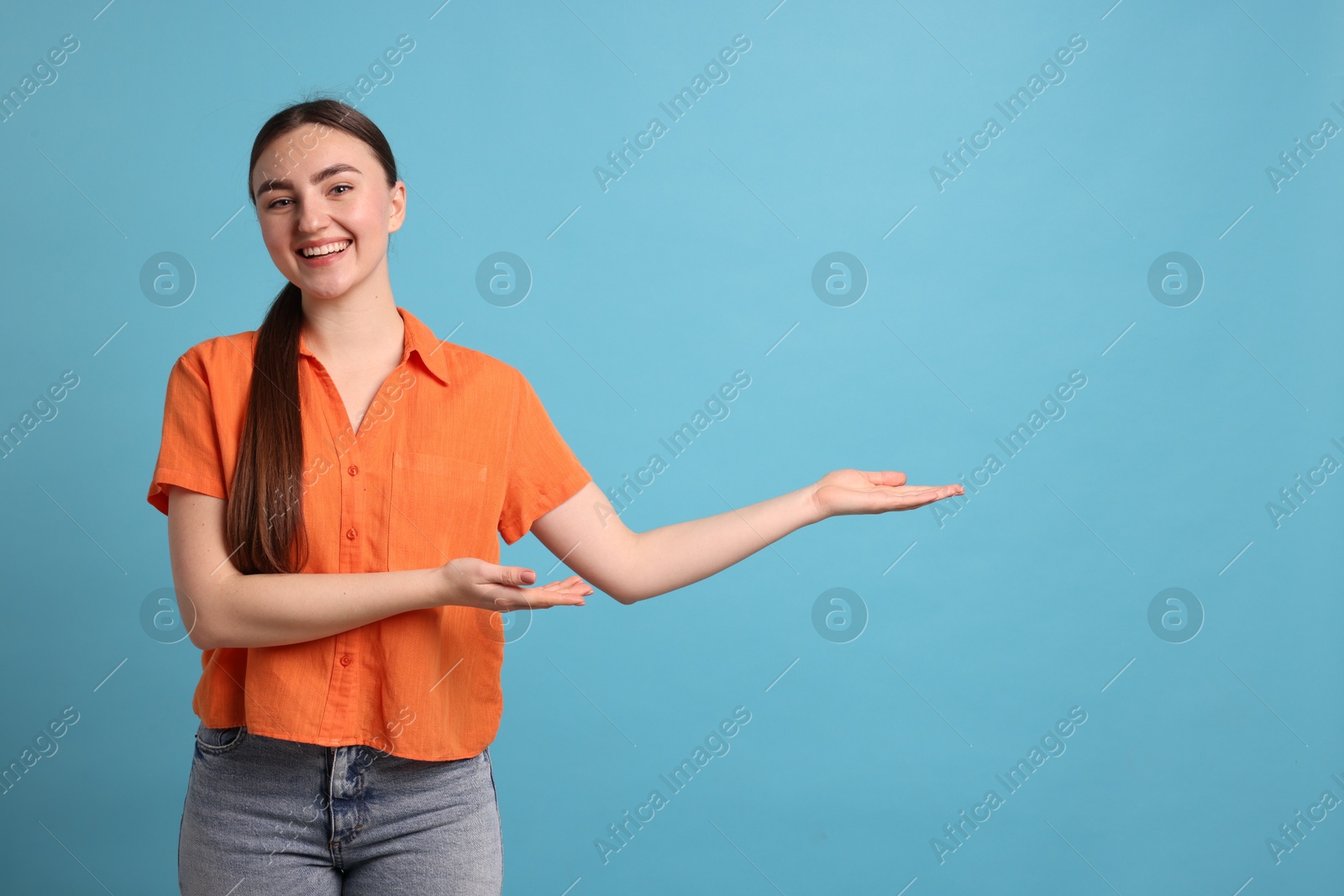 Photo of Cheerful woman welcoming guests on light blue background. Space for text