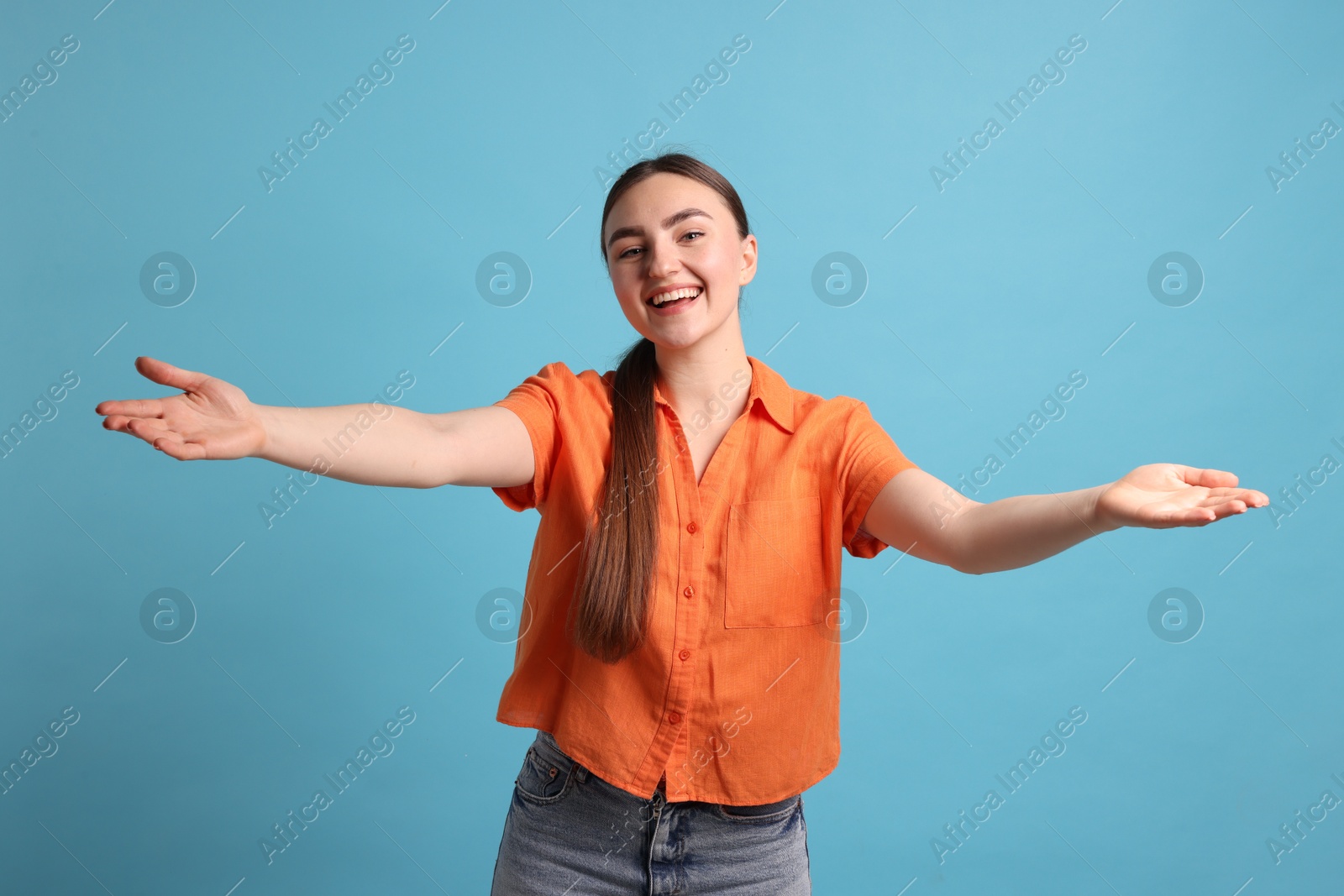 Photo of Cheerful woman welcoming guests on light blue background