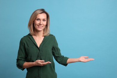 Photo of Cheerful woman welcoming guests on light blue background. Space for text