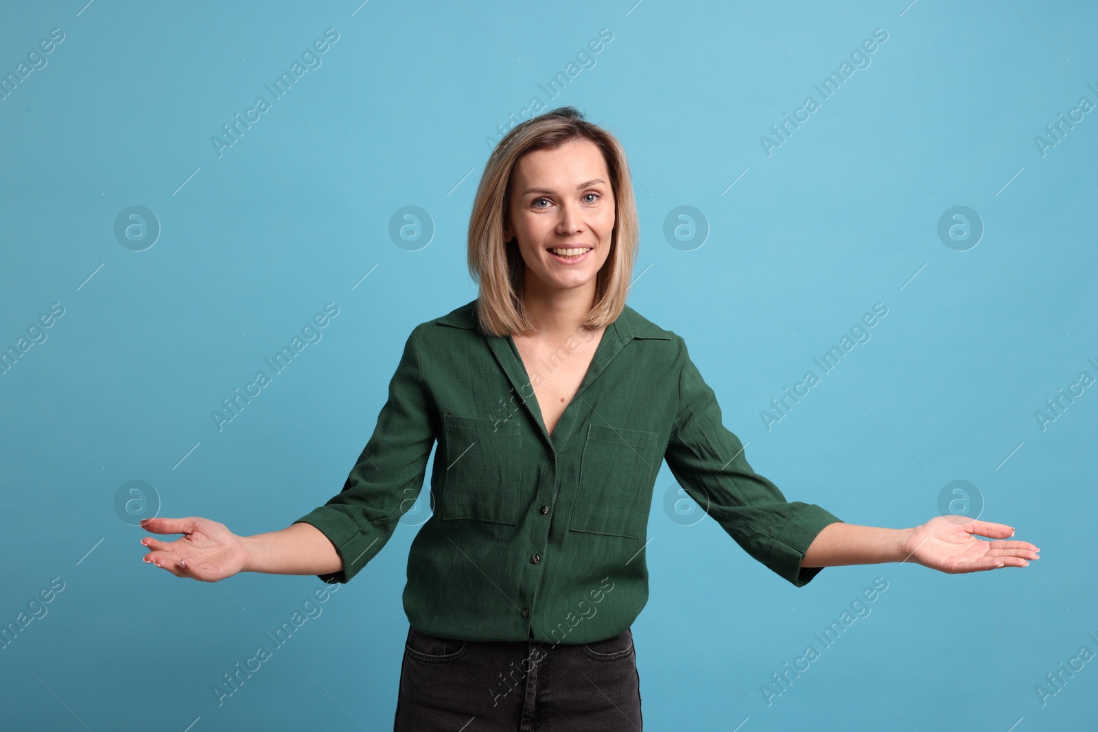 Photo of Cheerful woman welcoming guests on light blue background