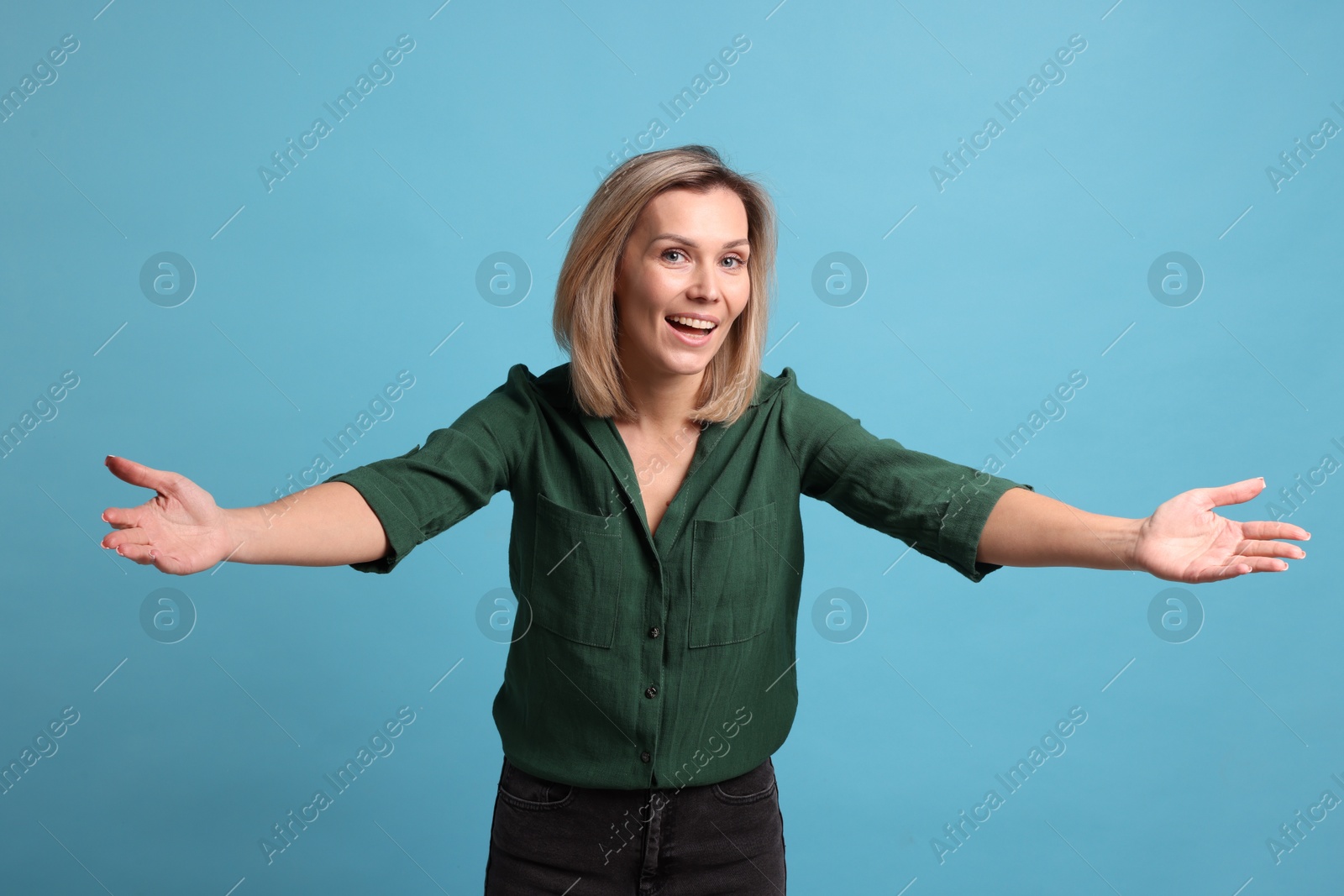 Photo of Cheerful woman welcoming guests on light blue background