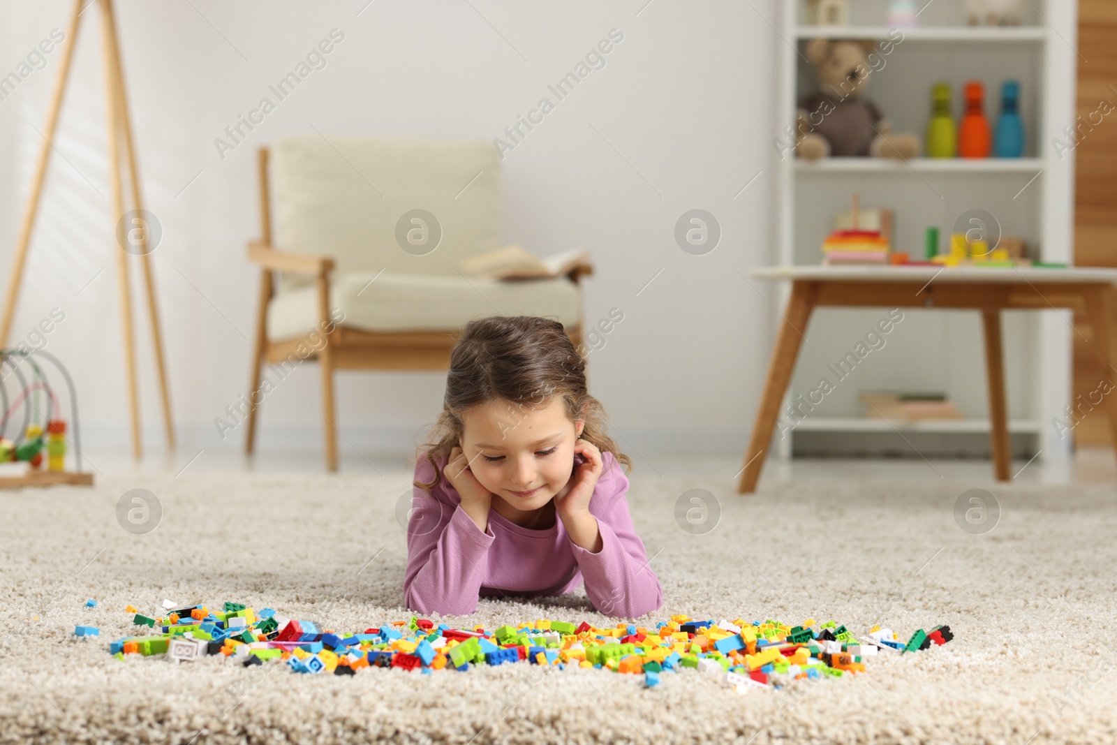 Photo of Cute girl playing with building blocks on floor at home