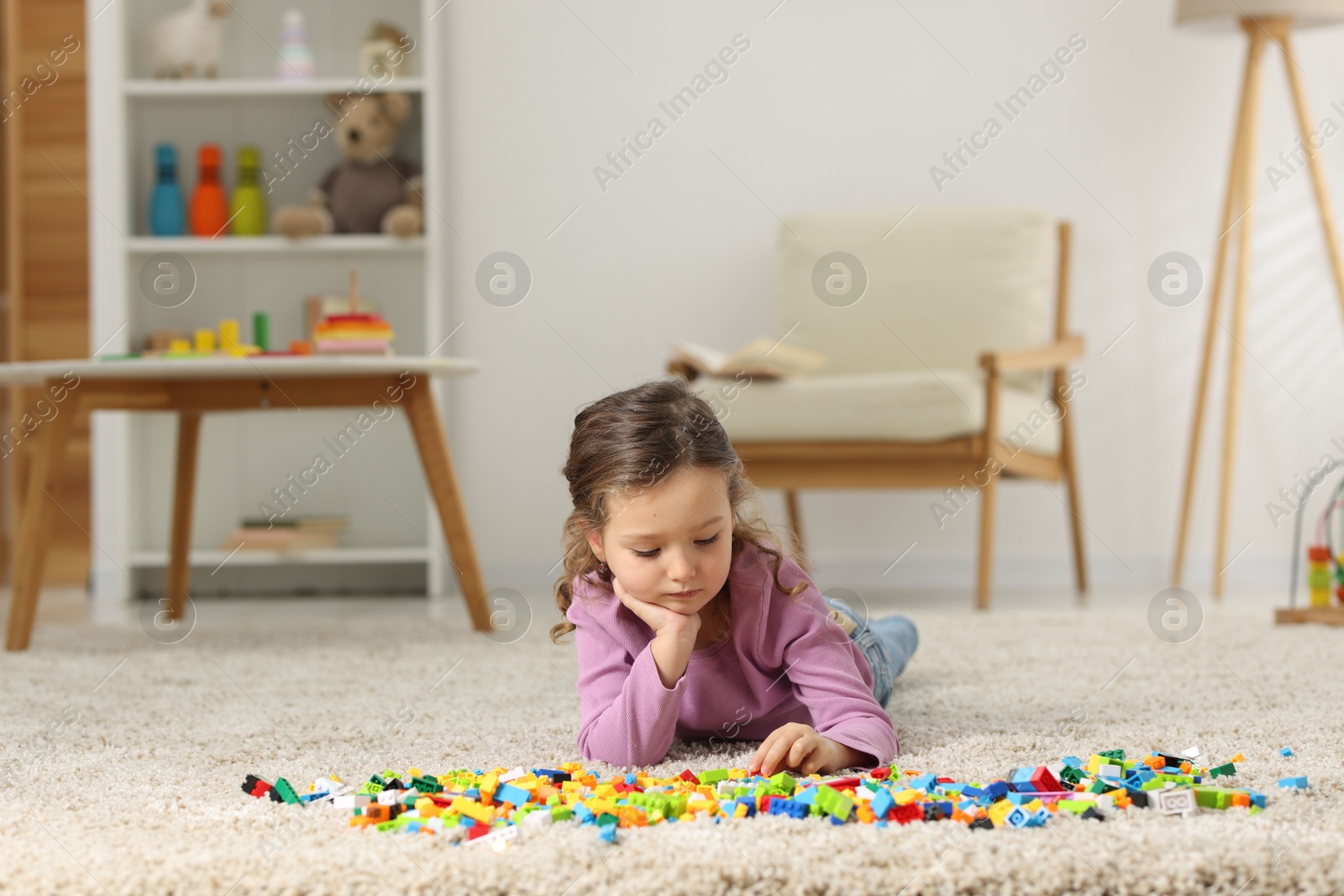 Photo of Cute girl playing with building blocks on floor at home