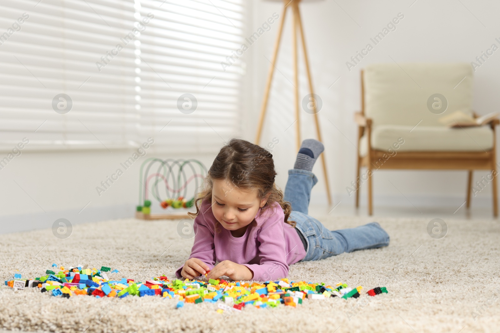 Photo of Cute girl playing with building blocks on floor at home